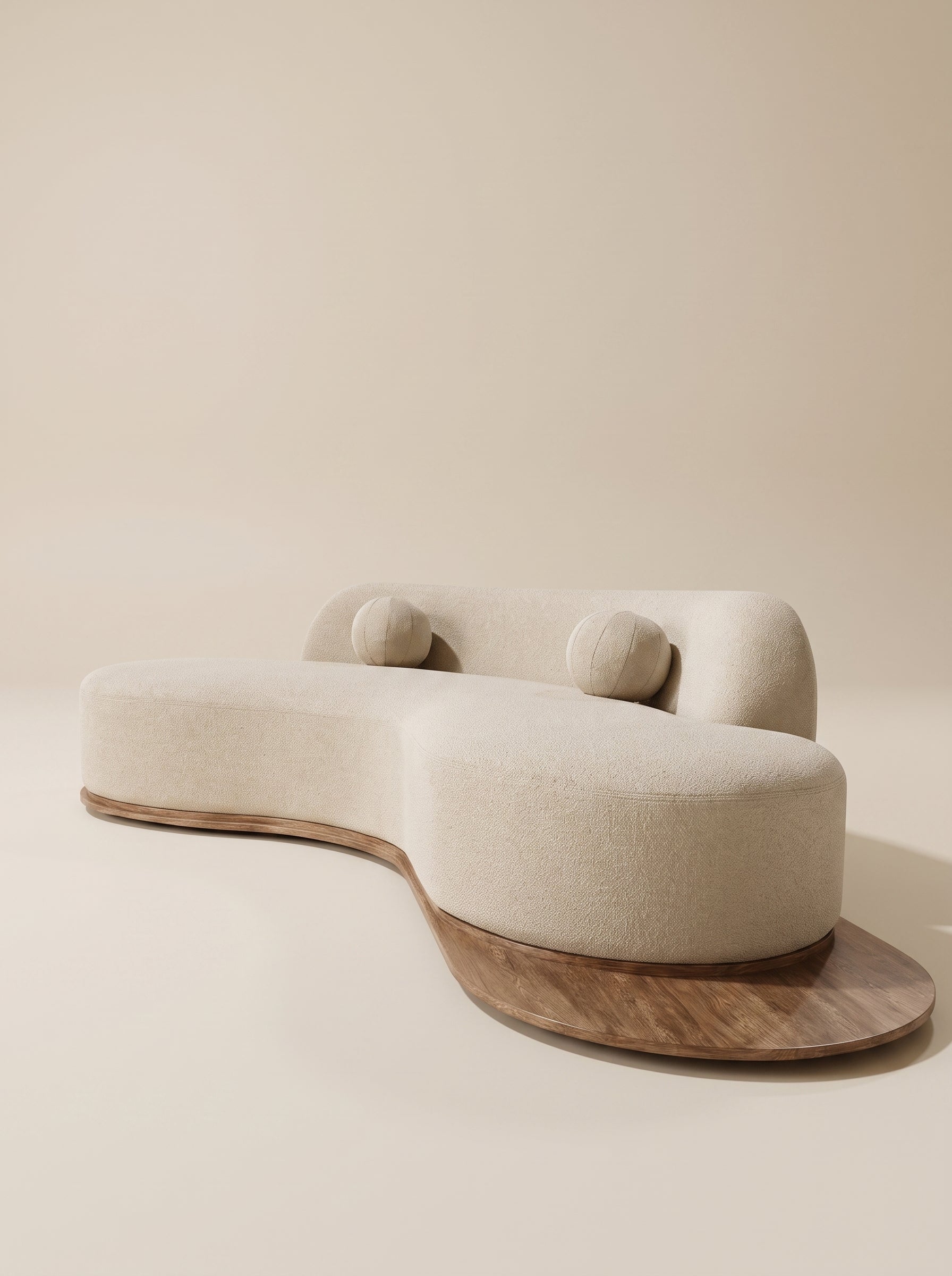Sofá curvo orgánico Ámbar tapizado en tela texturizada beige claro con base de madera natural extendida y dos cojines esféricos.