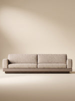 Sofá lineal de tres puestos Bali tapizado en tela texturizada beige con base inferior combinada en tono taupe y zócalo de madera natural.