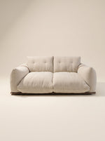 Sofá de dos plazas Cluddo de silueta mullida y perfil bajo tapizado en tela texturizada beige claro con base de madera a ras de suelo.