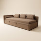 Vista frontal de un sofá cama de diseño lineal tapizado en tela texturizada tono café grisáceo (taupe), con respaldo bajo compuesto por tres cojines rectangulares con costura central, un apoyabrazos izquierdo con cojín cilíndrico y base frontal con dos tiradores para extracción de cama inferior, sobre fondo neutro de estudio.