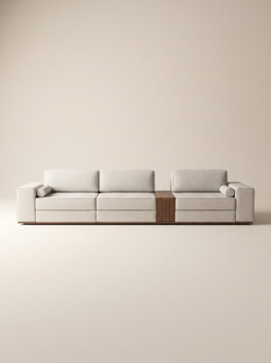 Sofá modular Reggio tapizado en tela neutra texturizada con mesa lateral integrada de madera natural y cojines cilíndricos sobre fondo blanco.