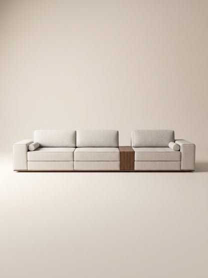 Sofá modular Reggio tapizado en tela neutra texturizada con mesa lateral integrada de madera natural y cojines cilíndricos sobre fondo blanco.