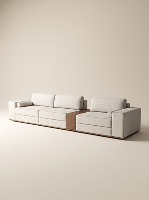 Sofá modular Reggio tapizado en tela neutra texturizada con mesa lateral integrada de madera natural y cojines cilíndricos sobre fondo blanco.