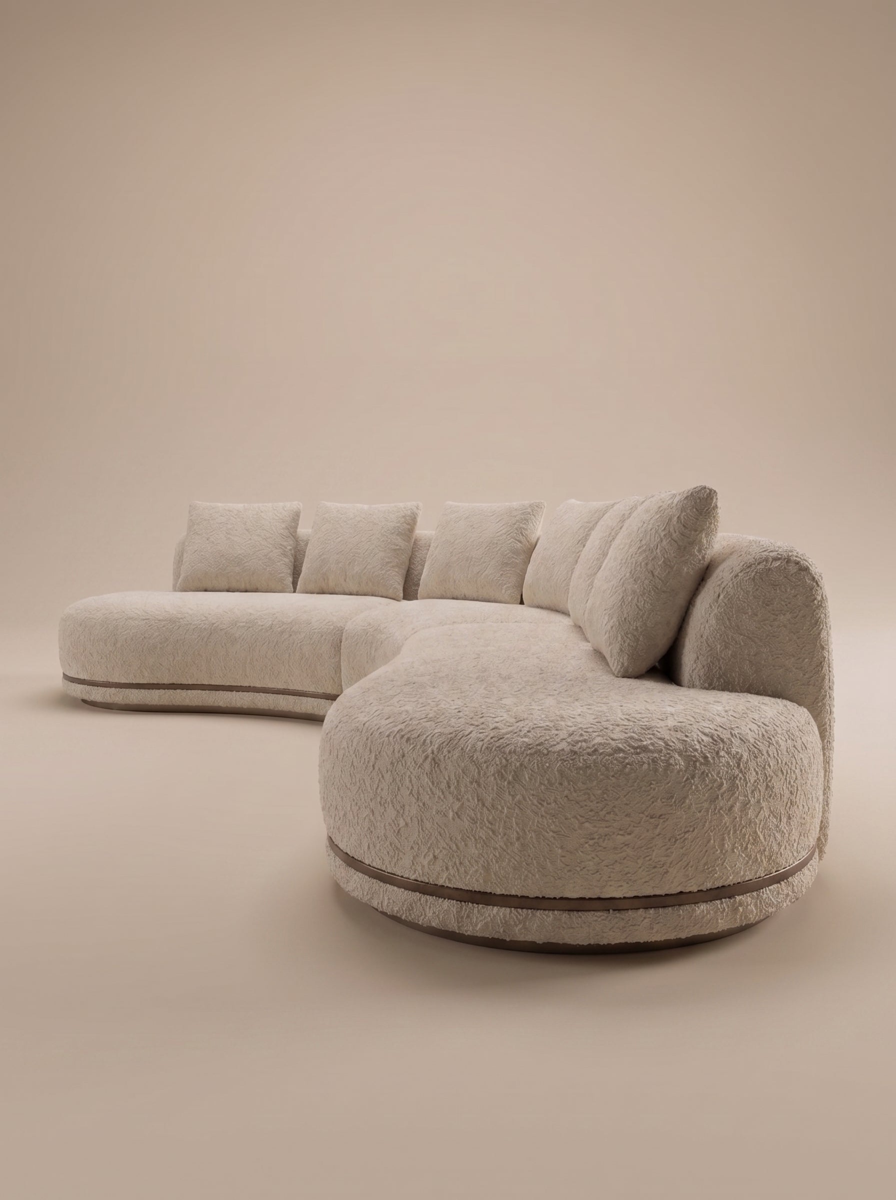 Vista frontal de un sofá modular curvo tapizado en tejido de borreguito (bouclé) de color beige claro. Cuenta con seis cojines cuadrados grandes en el respaldo y un pequeño cojín esférico a la izquierda. La base es de metal y madera con una franja de cuero marrón. El extremo derecho incluye una mesa auxiliar integrada de madera de nogal semicircular.